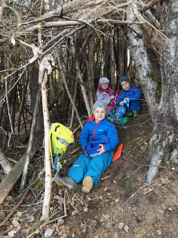 Kinder sitzen im Wald zwischen Ästen und essen ihre Jause