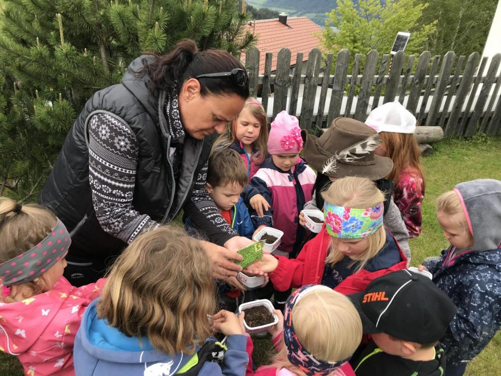 Kinder sammeln sich um unsere Assistentin um sich Kressesamen zu nehmen.