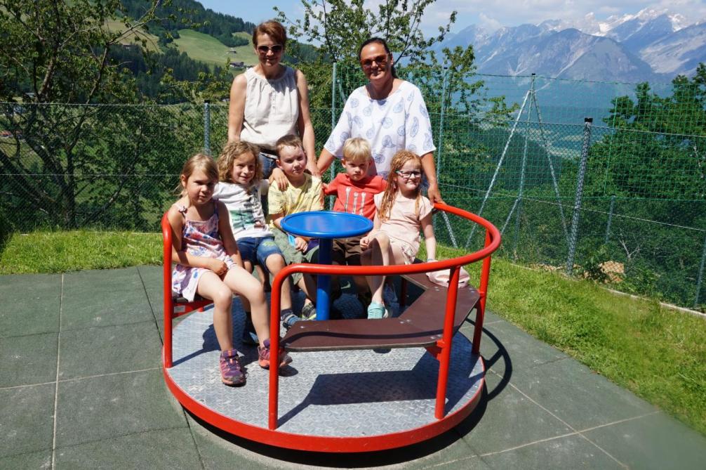Die Schulmäuse sitzen am Karusell des Spielplatzes, dahinter Barbara und Anna
